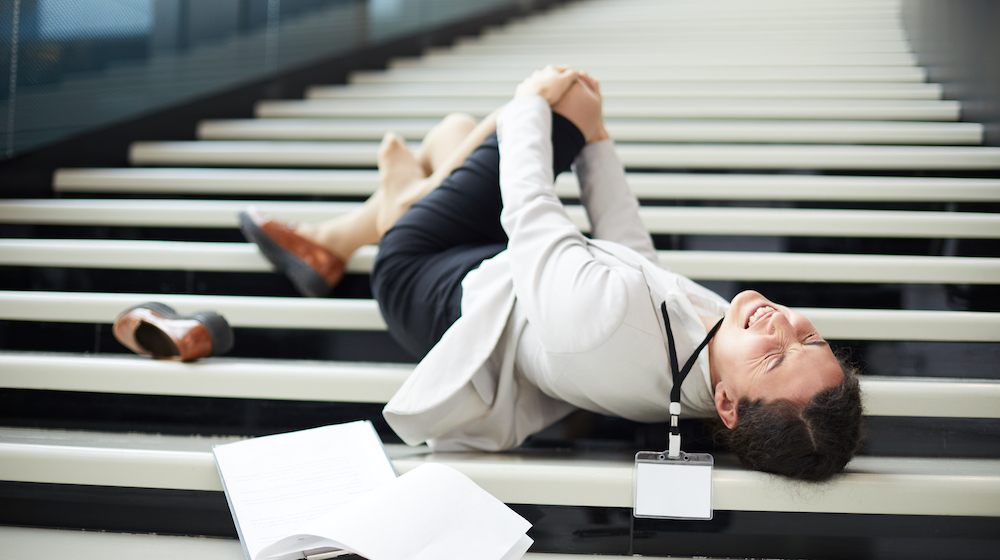 Sad young mixed race business lady feeling pain in knee lying on stair and holding knee, she falling down stairs